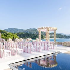 an outdoor wedding set up with pink and white flowers on the side of a swimming pool