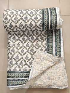 two pieces of white and blue patterned fabric on the floor next to one piece of cloth