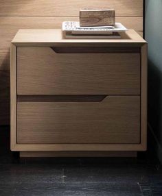 a wooden nightstand with two drawers next to a lamp on top of a table in front of a wall