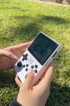 a person holding a nintendo wii game controller in their hand while sitting on the grass