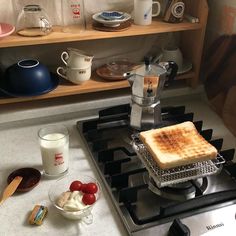 a toaster sitting on top of a stove next to cups and saucers in a kitchen