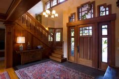 an entryway with stairs and rug on the floor in front of wooden doors, chandeliers and windows