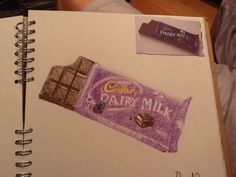 a drawing of a bar of chocolate on top of a notepad next to a person's hand