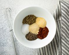 spices and seasonings in a white bowl next to a whisk on a towel