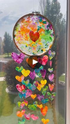 a colorful wind chime hanging from the side of a window with hearts painted on it