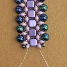 a purple and blue beaded brooch sitting on top of a wooden table next to a string