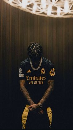 a man with dreadlocks standing in front of a wall wearing a black and yellow jersey