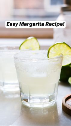 two glasses filled with ice and limes sitting on a counter next to sliced limes