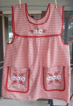 a red and white checkered dress hanging from a clothes line with flowers on it