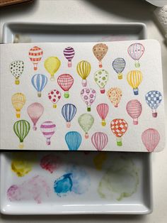 watercolors are being used to draw colorful hot air balloons on white paper with colored ink