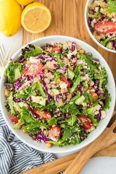 two white bowls filled with salad on top of a wooden cutting board next to lemons