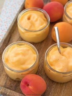 peaches and oranges are in small jars on a wooden tray with spoons