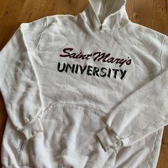 "This piece is a vintage hooded sweatshirt from the 1990s for Saint Mary's University in Halifax, Nova Scotia, Canada.  -Made in Canada, Monsport -55% Cotton, 45% Polyester -No Major Stains, Yellowing, or Flaws Tag Size: XL, fits slightly smaller *refer to measurements for true fit* Pit to Pit: 22.5\" Length: 28\" Please also assess the photos and measurements carefully using your own personal judgement as we do not accept returns. Keep in mind that this is a piece of vintage clothing that may hold a residual scent from its past. While we wash all of the clothing we sell (except for certain items which are steam cleaned) we cannot guarantee that we have been able to remove all of the stubborn scents. Buyers should be prepared for the possibility of having to wash the items again once they White Hooded Sweatshirt, University Hoodie, Halifax Nova Scotia, Saint Marys, Saint Mary, Nova Scotia, Vintage Sweatshirt, Vintage Clothing, Hooded Sweatshirt