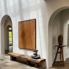 a large painting hangs on the wall next to a wooden bench in a white walled room