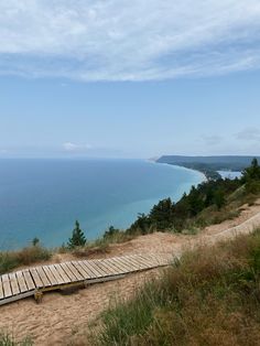 a wooden walkway leading to the ocean on top of a hill near grass and trees