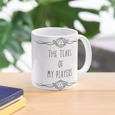 a white coffee mug with the words, the tears of my players on it next to some books