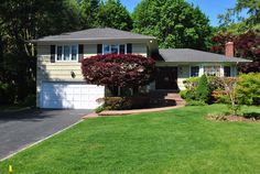 a house with trees and bushes in the front yard, on a sunny day that's just starting to turn green