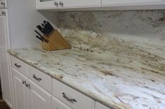 a marble counter top in a kitchen with white cabinets and cupboards behind it is a knife block that has been used as a holder for knives