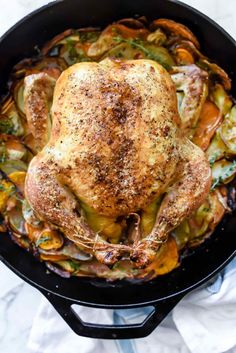 a roasted chicken in a cast iron skillet with vegetables and herbs on the side