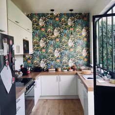 the kitchen is decorated with colorful wallpaper and white cabinets, along with wood flooring