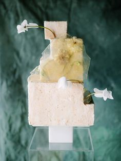 a piece of cake with flowers on it sitting on a glass stand in front of a green wall