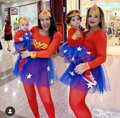 two women in wonder costume standing next to each other with one woman holding a baby