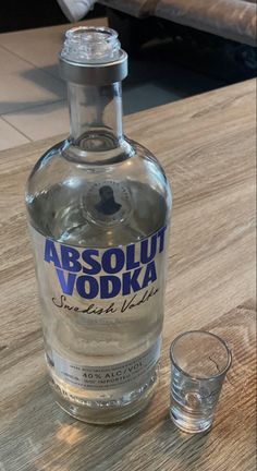 a bottle of absolut vodka next to an empty glass on a wooden table