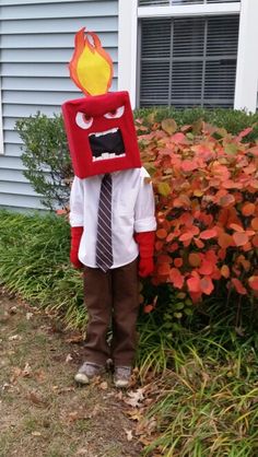 a young boy dressed up as a fireman standing in front of a bushes and shrubs