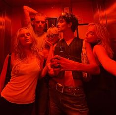 a group of young people standing around each other in a red light room holding wine glasses