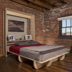 a bed sitting in the middle of a room next to a brick wall and wooden floors