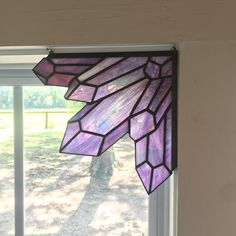 a purple stained glass window hanging from the side of a wall next to a tree