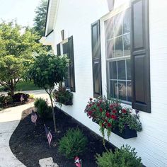 a white house with flowers in the window boxes and an american flag on the front lawn