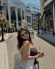 a woman is standing on the street with a bag and drink in her hand while smiling