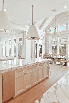 a large kitchen with marble counter tops and wooden cabinets in the center, along with two chandeliers hanging from the ceiling