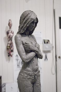 a sculpture of a woman with her hands on her chest in front of a white wall