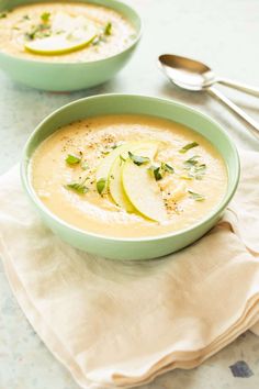 two green bowls filled with soup on top of a white cloth next to silver spoons