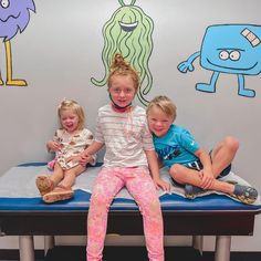 three children sitting on a bed in front of a wall with cartoon drawings and monsters