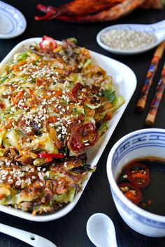 a plate with some food on top of it next to bowls and chopsticks