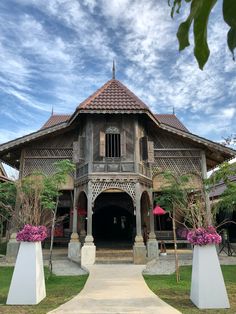 an old wooden building with pink flowers in the foreground