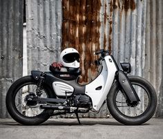 a white and black motorcycle parked in front of a rusty building with a helmet on it's seat