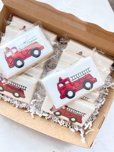 four decorated cookies in a cardboard box with frosting on the top and one cookie shaped like a firetruck