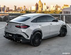 the rear end of a white mercedes suv parked in a parking lot with cityscape in the background