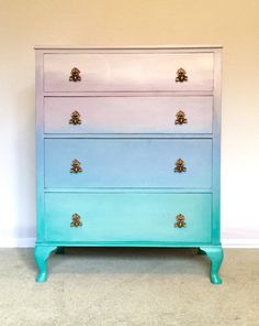 a blue and white dresser with gold knobs on the top, sitting against a wall