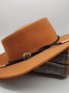 Elevate your cowboy hat style with our exquisite handcrafted hat band featuring a captivating oval Tigers Eye stone as its centerpiece. Each stone is meticulously polished to perfection, showcasing its natural beauty and warm glow. Designed to add a touch of elegance to your western look, this hat band is adorned with an oval silver-tone setting, creating a striking contrast against the rich hue of the stone. The band is crafted from black vegan cording, accented with fancy silver-tone "stacked" end caps. Hat bands are more than just accessories; they're a form of personal expression, reflecting your unique style and personality. As someone who grew up on the ranch, I understand the significance of these adornments. Adjustable to fit different hat sizes, this hat band offers versatility an Adjustable Hats For Rodeo, Adjustable Wide Brim Felt Hat For Western-themed Events, Adjustable Brimmed Top Hat For Western-themed Events, Adjustable Western Style Brimmed Fedora, Adjustable Wide Brim Felt Hat For Rodeo, Adjustable Brimmed Country Style Felt Hat, Adjustable Brimmed Country Felt Hat, Adjustable Fedora For Western-themed Events, Adjustable Wide Brim Felt Hat For Country Events