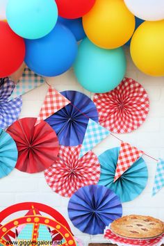 colorful balloons and paper fans are hanging from the ceiling above a table with pies