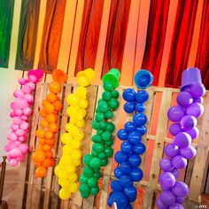 there are many balloons hanging on the wooden rack in front of the wall and behind them is a rainbow colored curtain