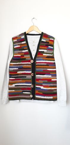 a white shirt and black vest with multicolored knits on it, hanging from a wooden hanger