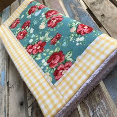 a close up of a piece of cloth on a wooden bench with flowers and gingham