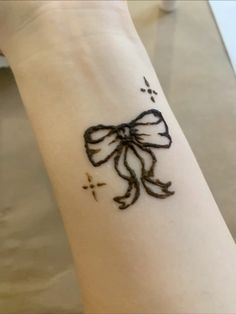 a tattoo on the wrist of a woman with a bow and cross drawn on it