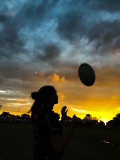 a woman is throwing a frisbee in the air at sunset with clouds behind her